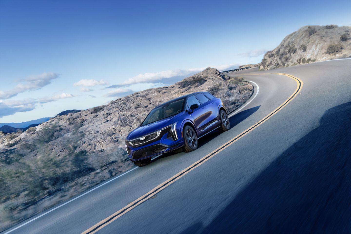 2026 Cadillac Optiq-V - A blue Cadillac Optiq-V driving on a winding mountain road - City Cadillac - New car dealership in Toronto, Ontario