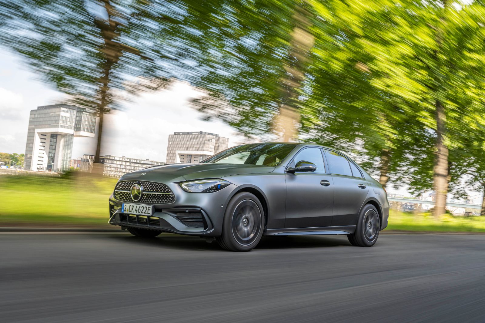 2025 Mercedes-Benz C-Class - A matte grey sedan driving on a tree-lined road - Mercedes-Benz Brampton - New car dealership in Toronto, Ontario