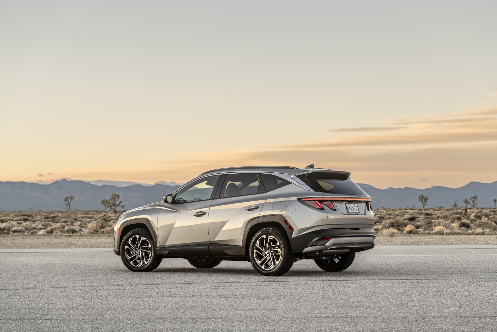 2025 Hyundai Tucson PHEV - the rear three-quarter view of a silver 2025 Hyundai Tucson PHEV parked in a desert at sunset - Humberview Group - new car dealerships in Ontario