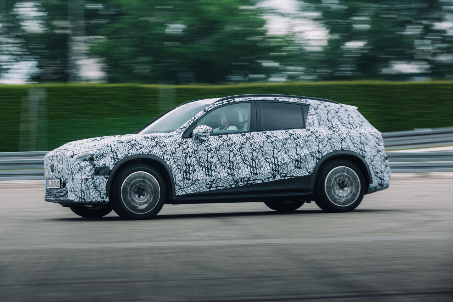 Mercedes-Benz GLC EQ - a side profile view of a black-and-white camouflaged Mercedes-Benz GLC EQ prototype driving on a test track - Mercedes-Benz Brampton - New car dealership in Brampton, Ontario