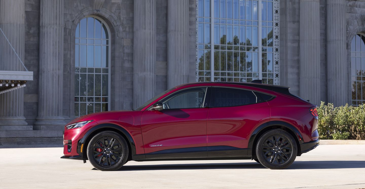 2026 Ford Mustang Mach-E - Side profile view of a red 2026 Ford Mustang Mach-E parked in front of a stone building - Mayfield Ford - New car dealership in Brampton, Ontario
