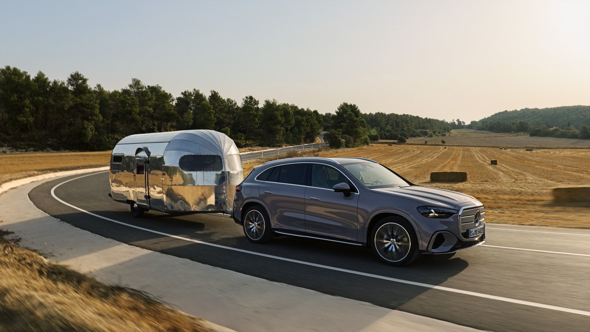 2026 Mercedes-Benz GLC with EQ Technology - A grey SUV towing a silver travel trailer on a winding country road - Mercedes-Benz Brampton - New car dealership in Brampton, Ontario