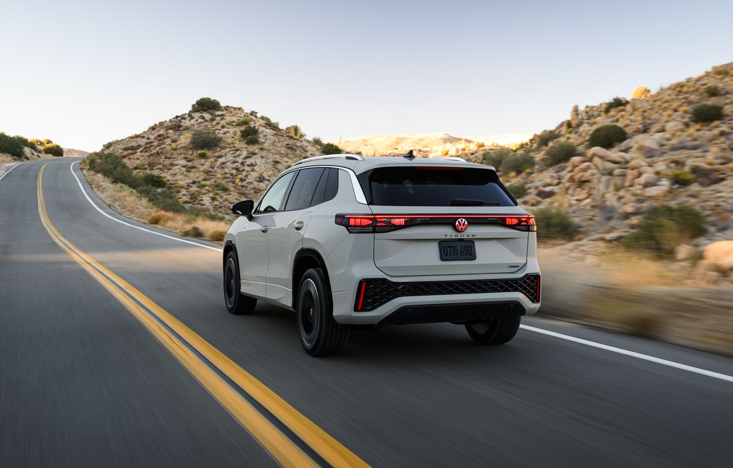 2026 Volkswagen Tiguan - Rear three-quarter view of a light grey 2026 Volkswagen Tiguan driving on a paved mountain road - Humberview Volkswagen - New car dealership in Toronto, Ontario