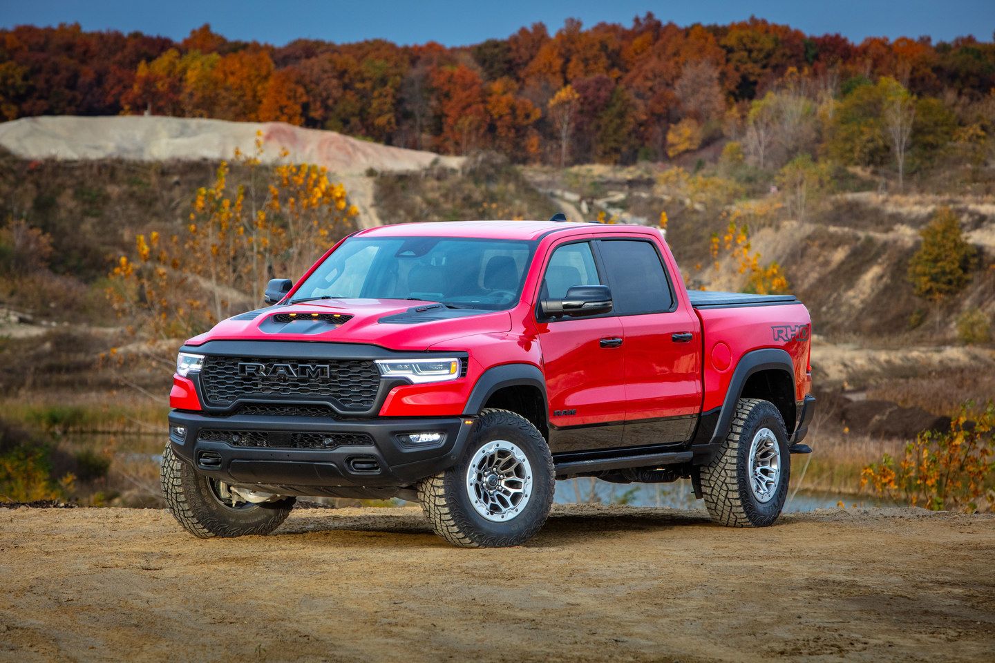 2026 Ram 1500 RHO - a red 2026 Ram 1500 RHO parked on a dirt hill in an off-road setting with autumn foliage in the background - Cooksville Dodge Chrysler - New car dealership in Mississauga, Ontario