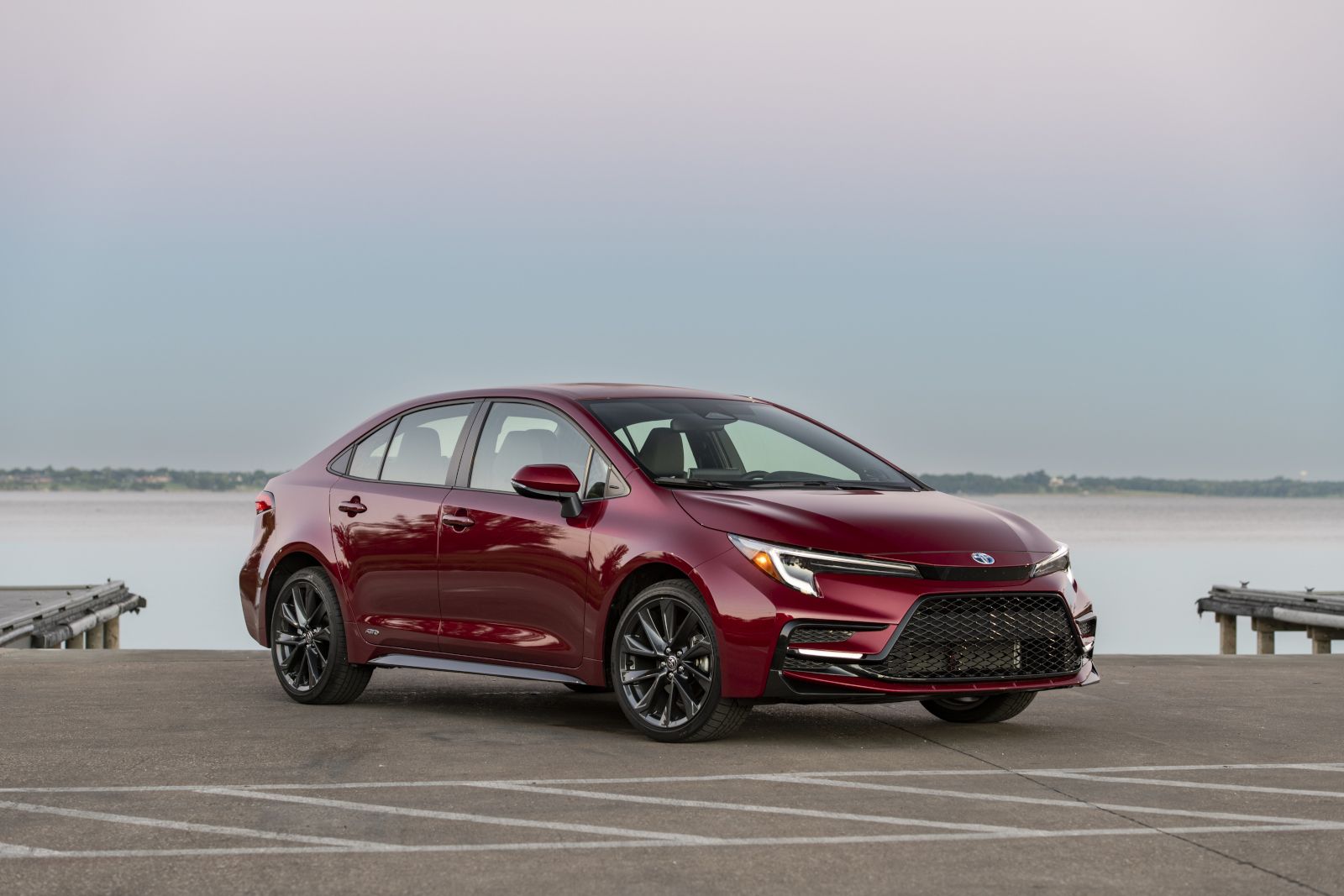 2026 Toyota Corolla Hybrid - Front three-quarter view of a red 2026 Toyota Corolla Hybrid parked on a pier - Oakville Toyota - New car dealership in Oakville, Ontario