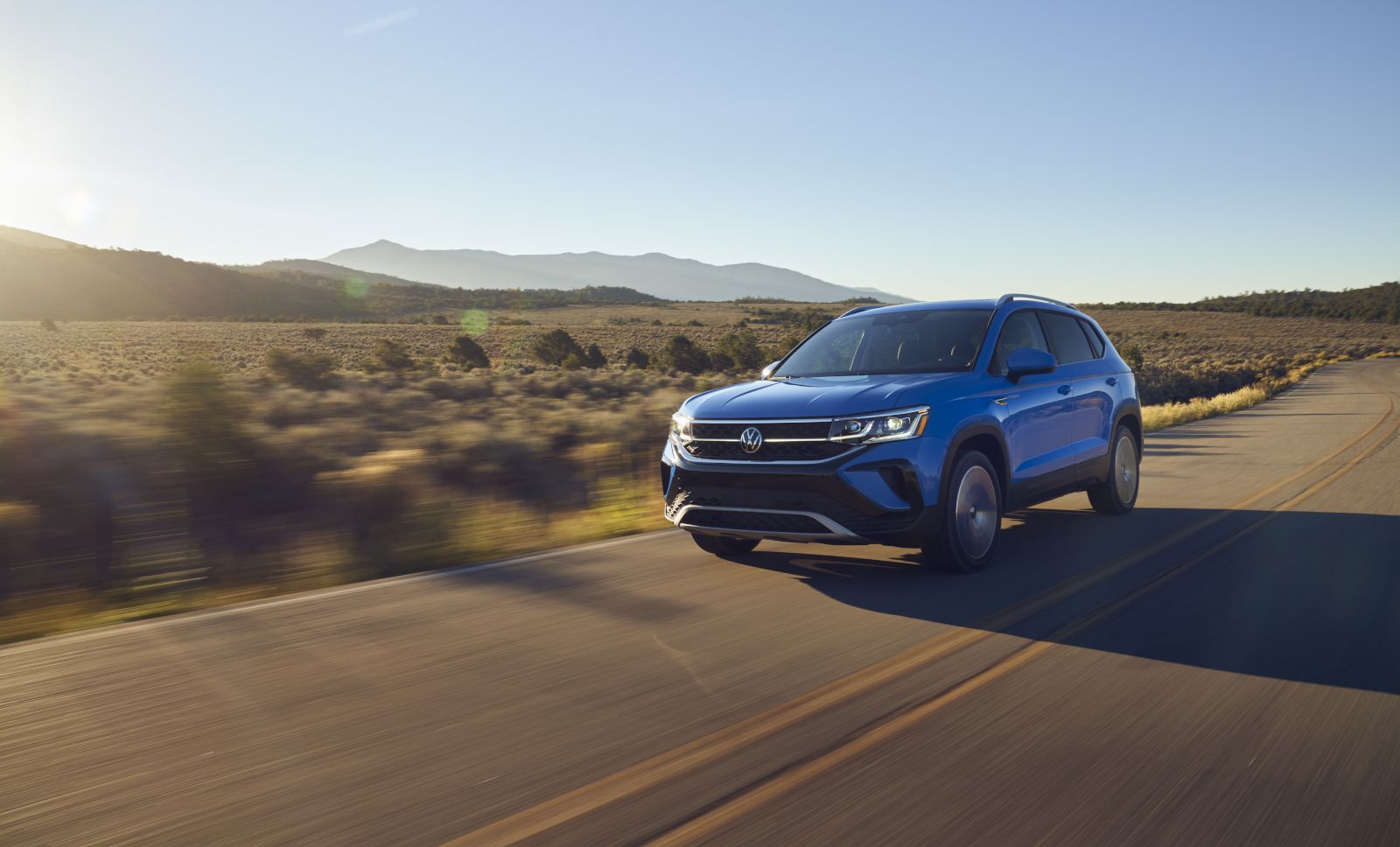 Volkswagen Taos - A blue Volkswagen Taos driving on a scenic road at sunrise - Autopark Barrie - Used car dealership in Barrie, Ontario