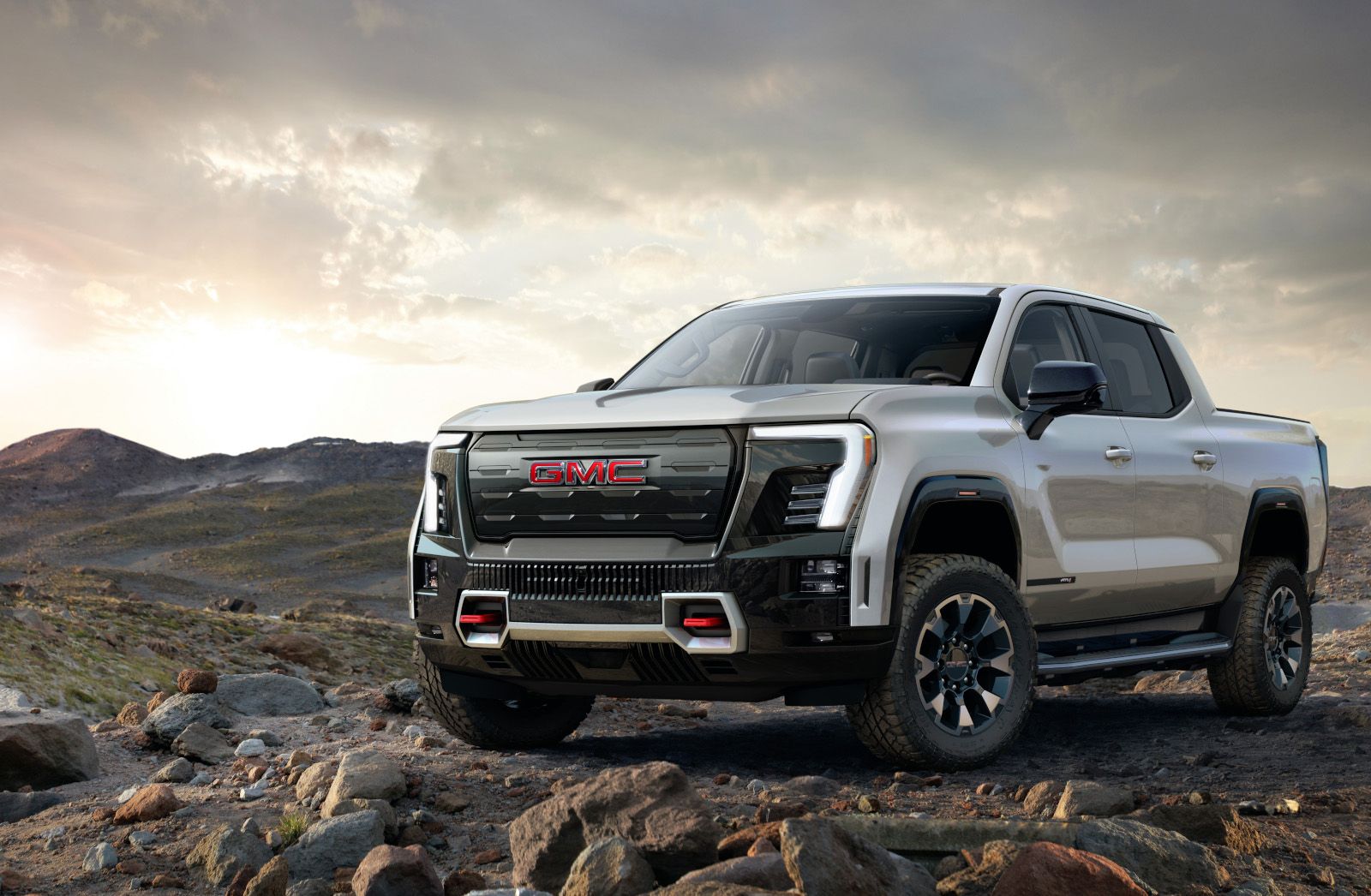 2026 GMC Sierra EV - a silver 2026 GMC Sierra EV parked on a rocky, off-road terrain at sunset - Applewood Chevrolet Buick GMC - New car dealership in Mississauga, Ontario