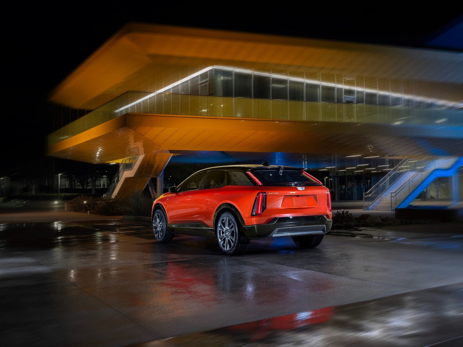 2026 Cadillac Optiq - Rear view of an orange 2026 Cadillac Optiq parked in front of a modern building at night.