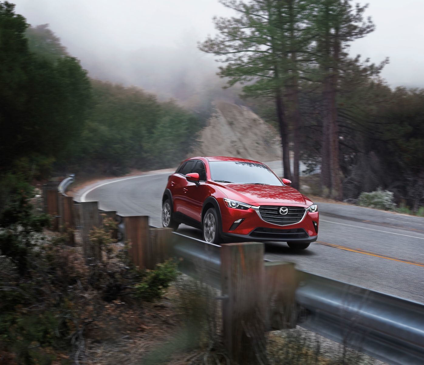 Mazda CX-3 - A red Mazda CX-3 driving on a winding, foggy mountain road - AutoPark Barrie - Used car dealership in Barrie, Ontario