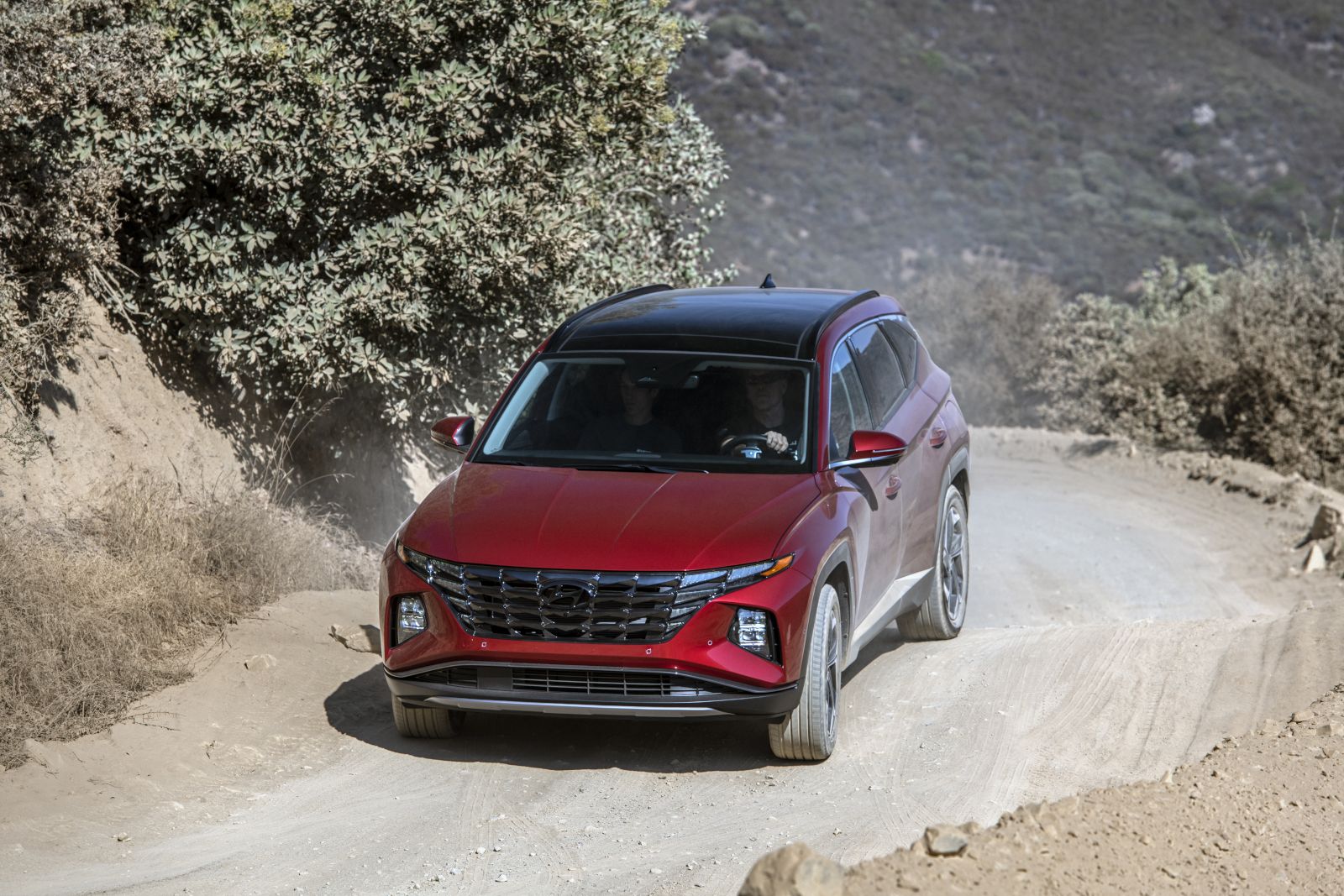 Hyundai Tucson - A red Hyundai Tucson with a black roof driving on a dirt road, shown from the front-three-quarter angle - AutoPark Brampton - Used car dealership in Brampton, Ontario
