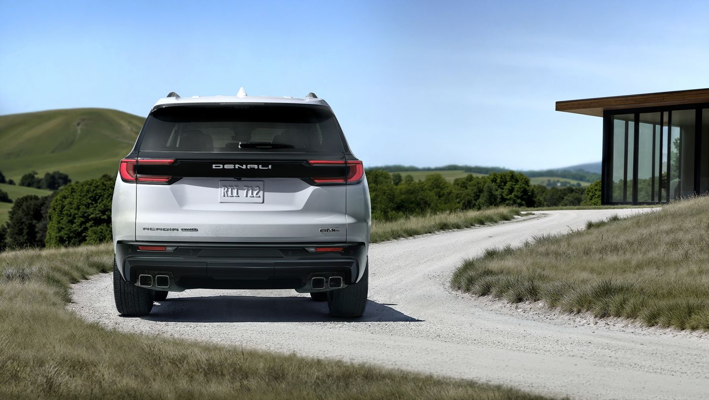 2026 GMC Acadia Denali - Rear view of a white GMC Acadia Denali on a country road.