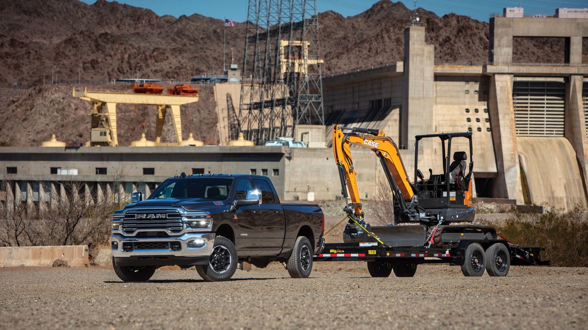 2026 Ram 2500 Heavy Duty - A dark grey Ram 2500 Heavy Duty towing an excavator on a trailer near a dam - Cooksville Dodge Chrysler Jeep RAM - New car dealership in Mississauga, Ontario