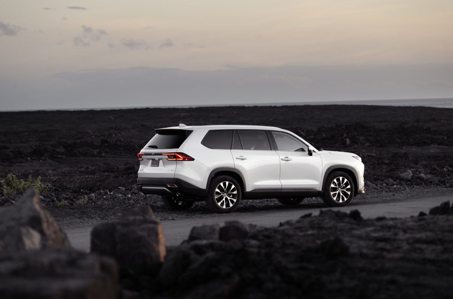 2026 Toyota Grand Highlander - Rear view of a white 2026 Toyota Grand Highlander driving on a road in a rocky landscape - Orangeville Toyota - Toyota new car dealership in Orangeville, Ontario