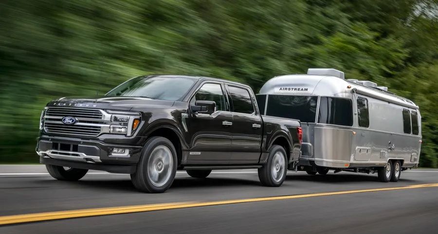 2026 Ford F-150 PowerBoost - A black Ford F-150 towing a large silver trailer on a road - Bayfield Ford - Ford car dealership in Barrie, ON