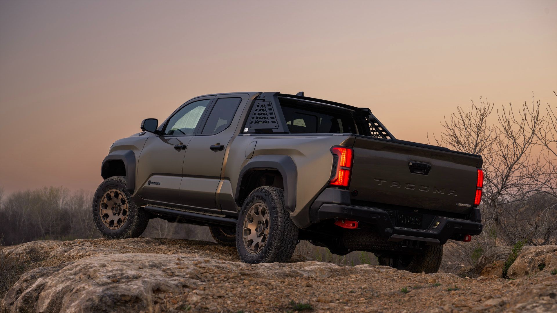 2026 Toyota Tacoma - Rear view of a bronze Trailhunter model parked on rocks at dusk - Goderich Toyota - New car dealership in Goderich, Ontario