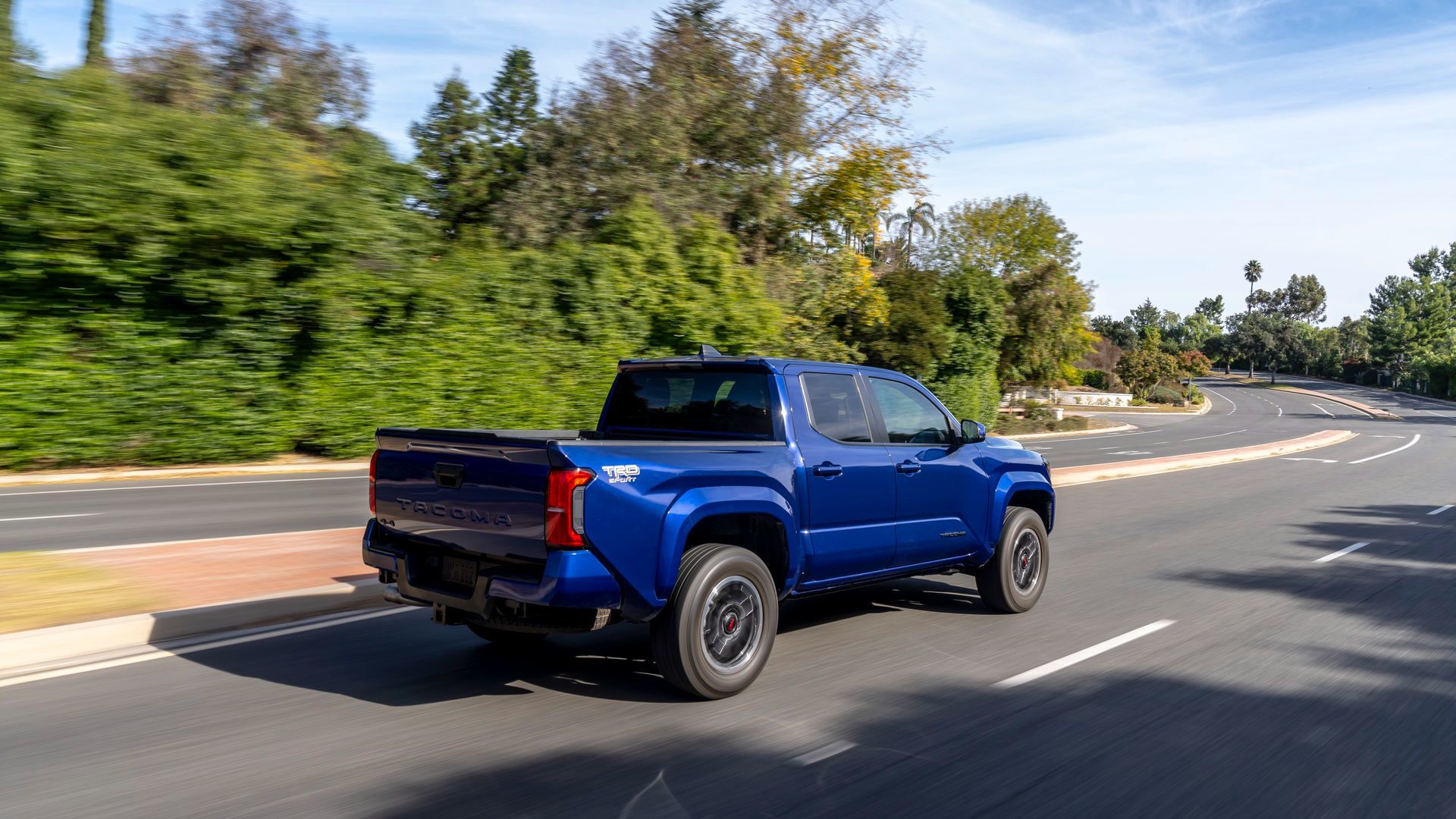 2026 Toyota Tacoma - Rear three-quarter view of a blue TRD Sport model driving on a paved road - Goderich Toyota - New car dealership in Goderich, Ontario