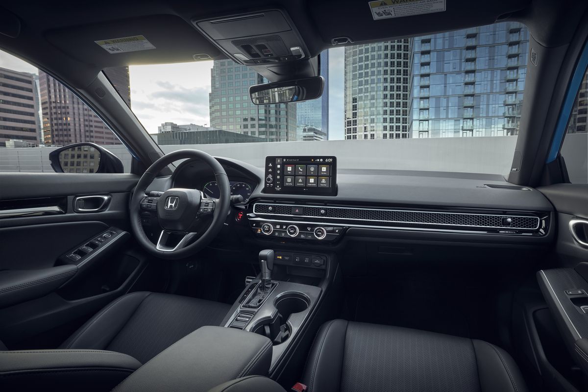 2026 Honda Civic Hatchback Hybrid - interior view of the dashboard and steering wheel with a city background - Goderich Honda - New car dealership in Goderich, Ontario
