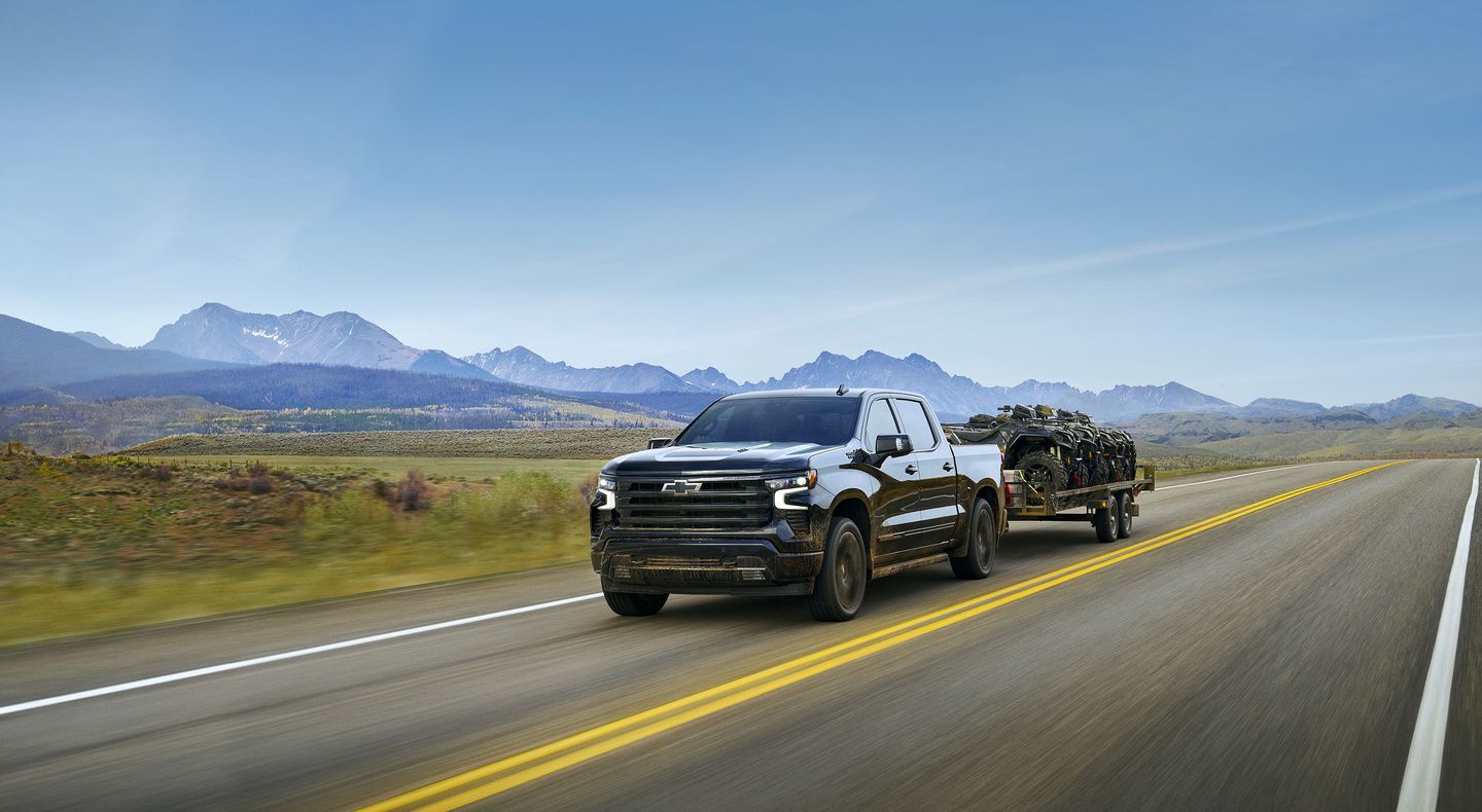2026 Chevrolet Silverado - front view of a black truck towing a trailer with ATVs.