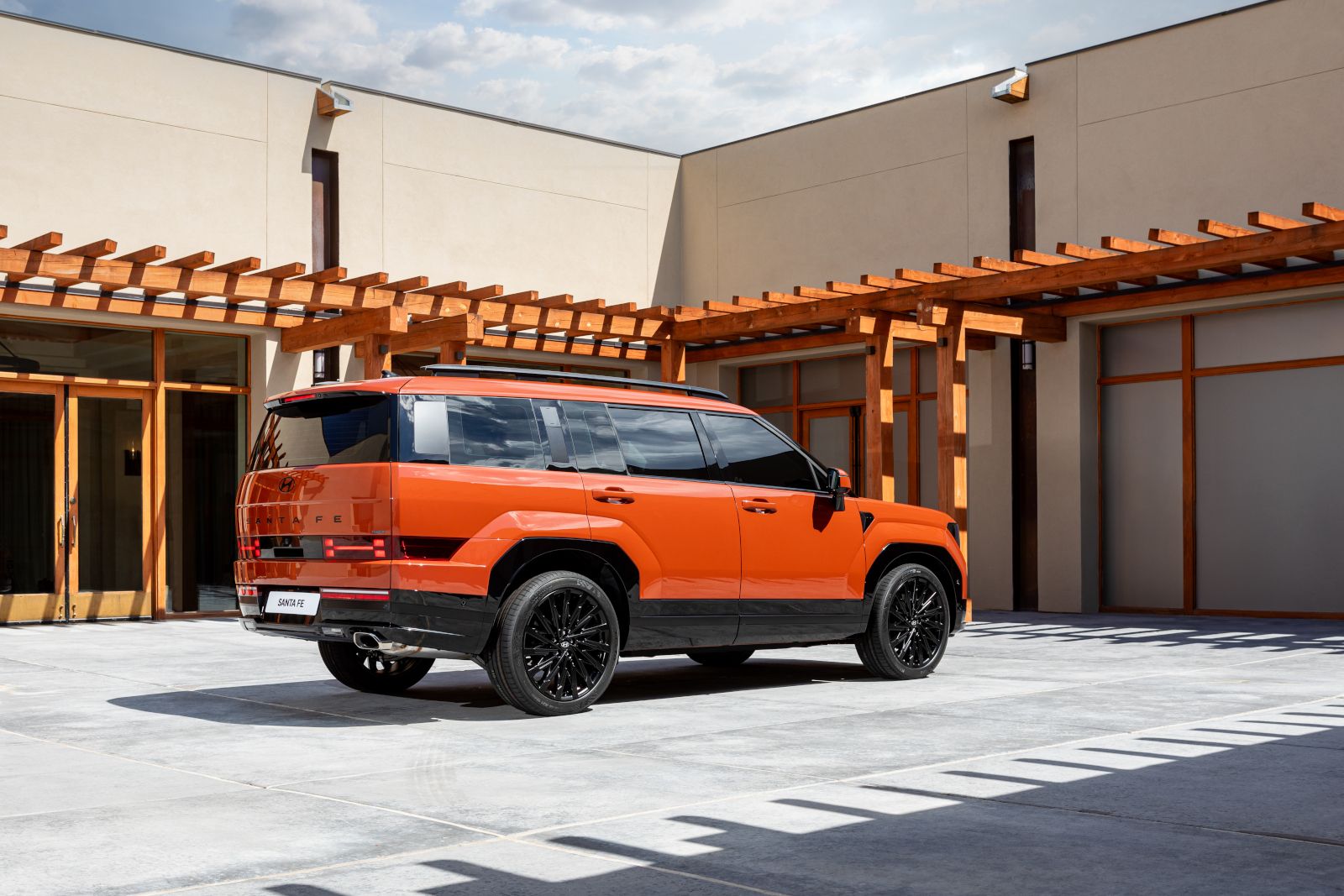 2026 Hyundai Santa Fe - rear three-quarter view of an orange 2026 Hyundai Santa Fe parked in a modern courtyard - Cooksville Hyundai - New car dealership in Mississauga, Ontario