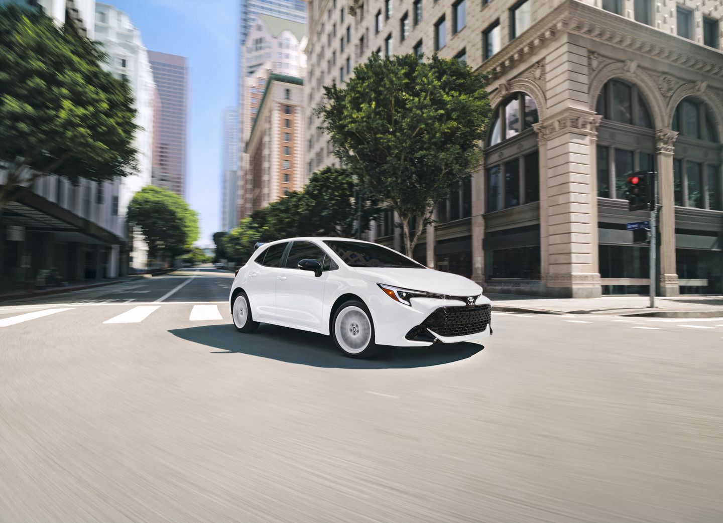 2026 Toyota Corolla Hatchback FX - a white 2026 Toyota Corolla Hatchback FX driving on a city street - Orangeville Toyota - Toyota car dealership in Orangeville, Ontario