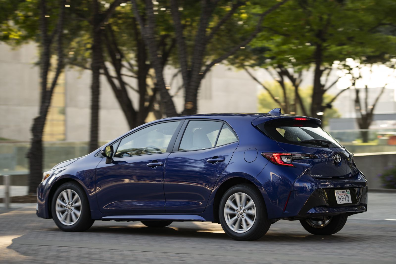 2026 Toyota Corolla Hatchback - side and rear view of a blue 2026 Toyota Corolla Hatchback driving on a street - Orangeville Toyota - Toyota car dealership in Orangeville, Ontario