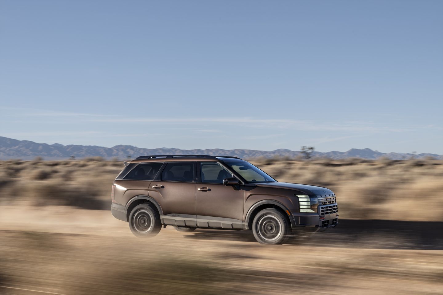 2026 Hyundai Palisade - a brown 2026 Hyundai Palisade driving on a dirt road - Woodstock Hyundai - New car dealership in Woodstock, Ontario