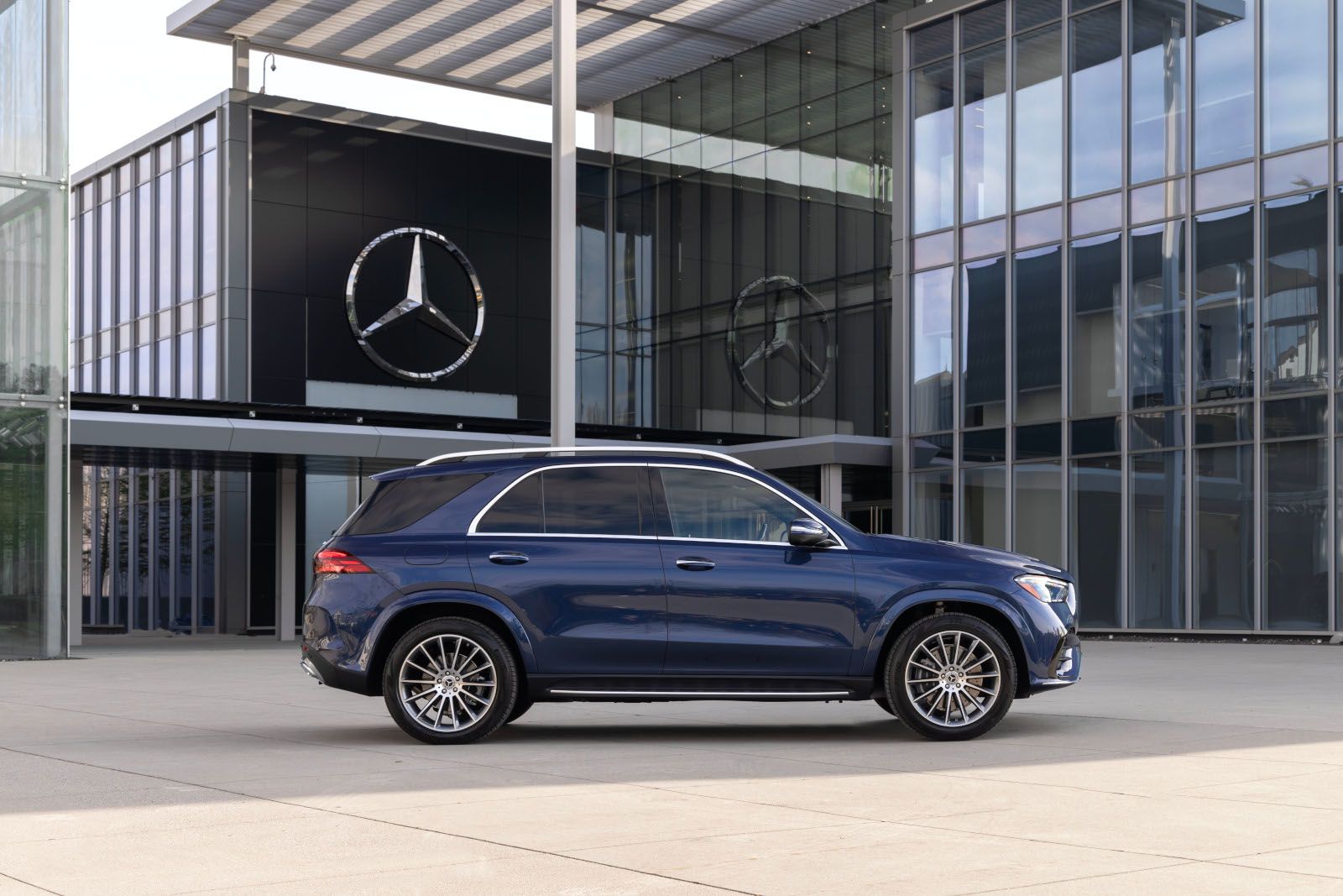 2026 Mercedes-Benz GLE - side profile view of a dark blue 2026 Mercedes-Benz GLE SUV parked in front of a modern building - Mercedes-Benz Brampton - New car dealership in Brampton, Ontario
