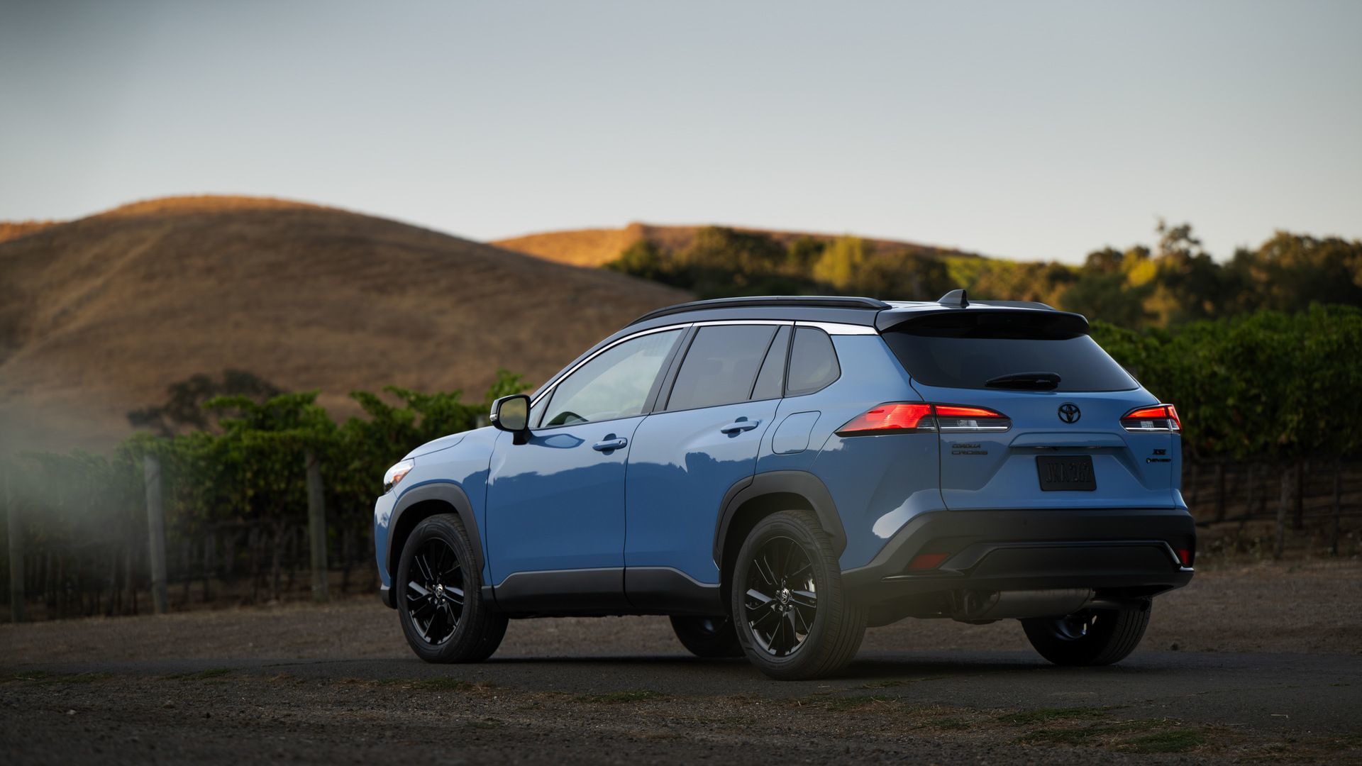 2026 Toyota Corolla Cross Hybrid - rear angle view of a Cavalry Blue 2026 Toyota Corolla Cross Hybrid parked on a scenic road - Oakville Toyota - New car dealership in Oakville, Ontario