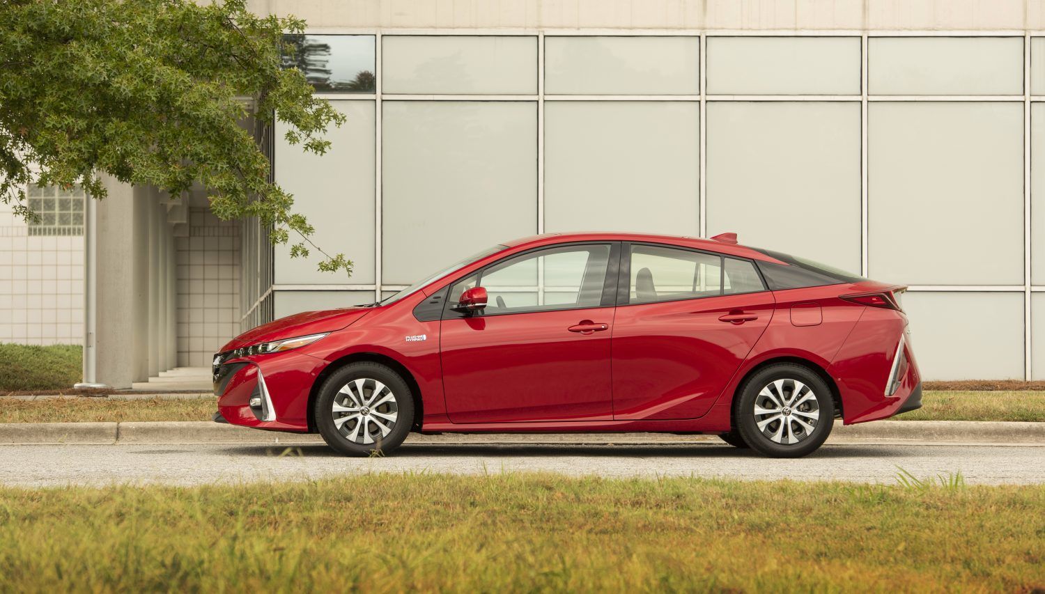 2020 Toyota Prius Prime - side profile view of a red 2020 Toyota Prius Prime parked in front of a modern glass building - Autopark Barrie - Used car dealership in Barrie, Ontario