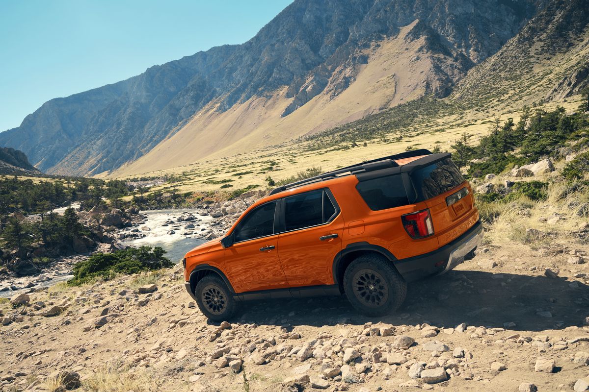 2026 Honda Passport - an orange 2026 Honda Passport TrailSport driving on a rocky trail with a river and mountains in the background - Humberview Group - New car dealerships in Ontario
