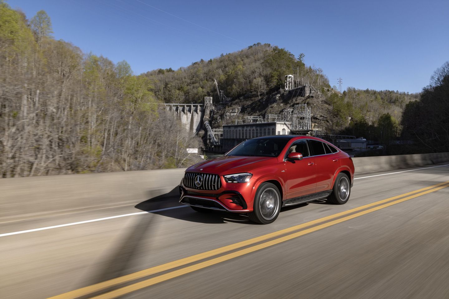 2026 Mercedes-Benz GLE - a red 2026 Mercedes-Benz GLE Coupe driving on a highway with a dam and forest in the background - Humberview Group - New car dealerships in Ontario