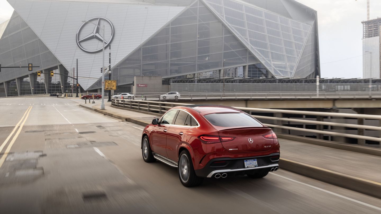 2026 Mercedes-Benz GLE 53 AMG Coupe - A red 2026 Mercedes-Benz GLE 53 AMG Coupe driving on a city bridge with a stadium in the background - Mercedes-Benz Brampton - New car dealership in Brampton, Ontario