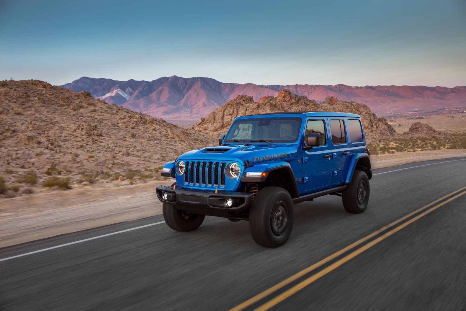 2026 Jeep Wrangler Rubicon - a blue 2026 Jeep Wrangler Rubicon driving on a paved road with mountain views - Cooksville Dodge Chrysler - New car dealership in Mississauga, Ontario