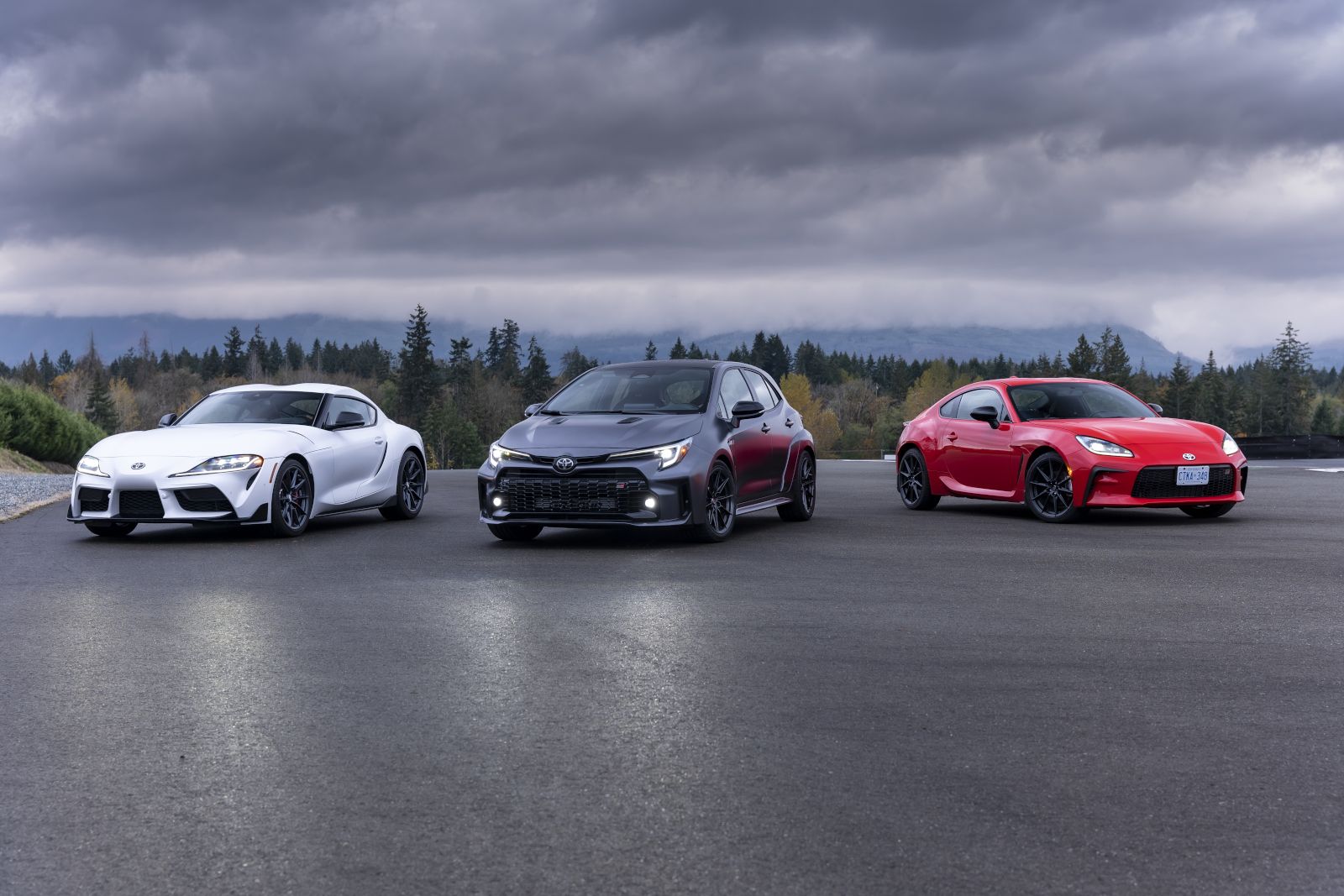2026 Toyota GR Supra, GR Corolla, and GR86 - a white GR Supra, grey GR Corolla, and red GR86 parked on an asphalt track - Goderich Toyota - Toyota new car dealership in Goderich, Ontario