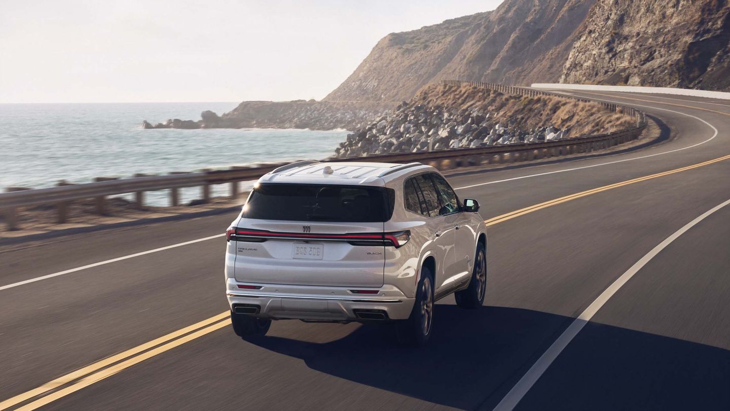 2026 Buick Enclave - rear 3/4 view of a white 2026 Buick Enclave driving along a scenic coastal highway - Applewood Chevrolet Buick GMC - Buick new car dealership in Mississauga, Ontario