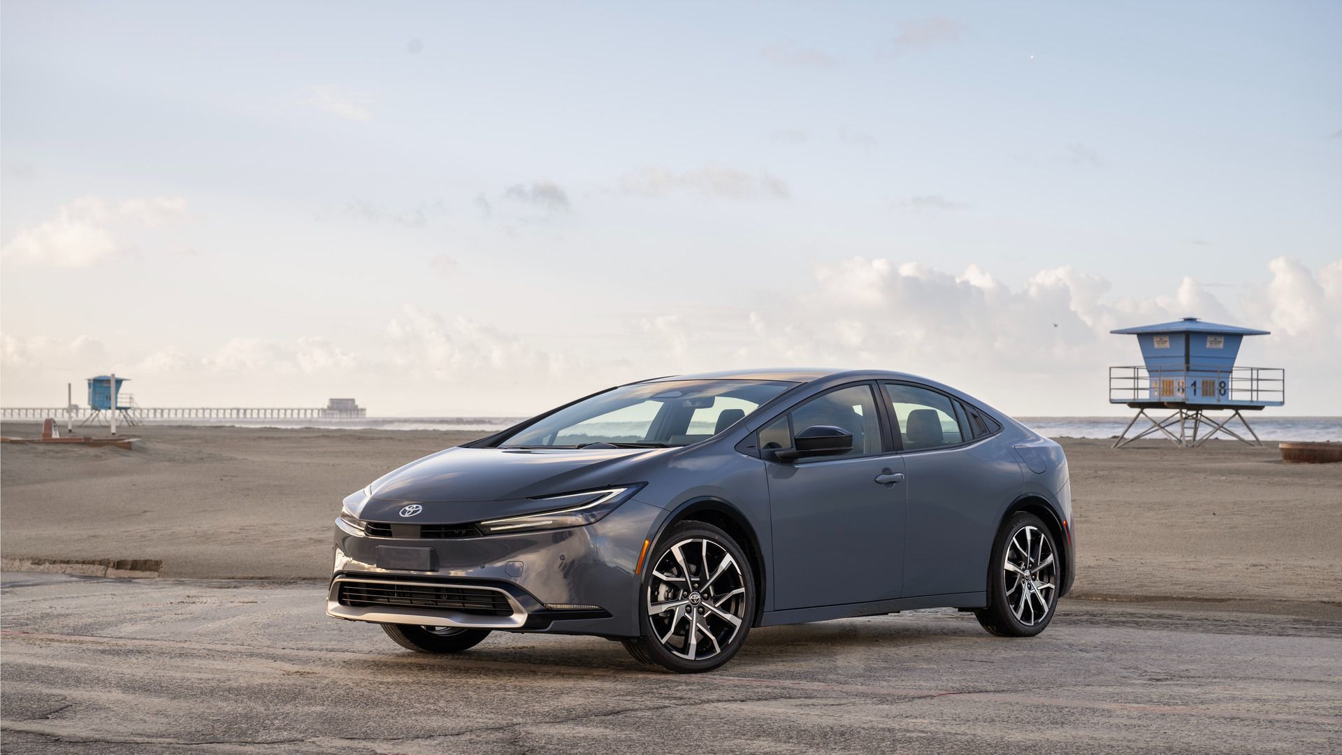 2026 Toyota Prius Prime - a grey 2026 Toyota Prius Prime parked on a beach with a lifeguard tower and pier in the background - Humberview Group - New car dealerships in Ontario