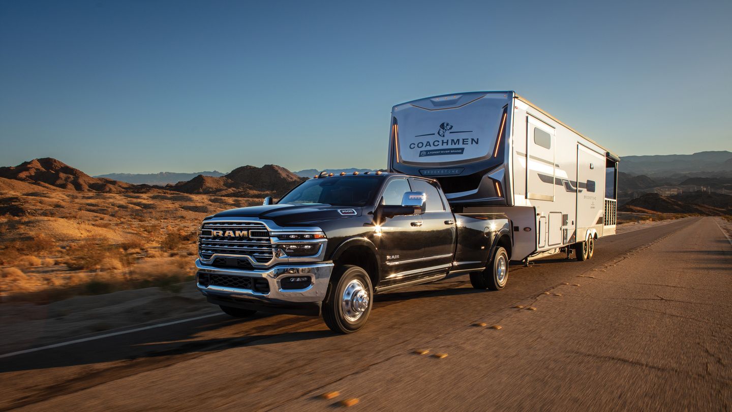 2026 RAM 3500 Limited - a black 2026 RAM 3500 Limited dually towing a large fifth-wheel trailer on a desert highway - Cooksville Dodge - RAM car dealership in Mississauga, Ontario