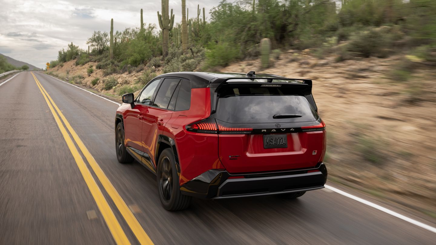 2026 Toyota RAV4 PHEV GR Sport - rear 3/4 view of a red 2026 Toyota RAV4 PHEV GR Sport driving on an open road - Oakville Toyota - Toyota new car dealership in Oakville, Ontario