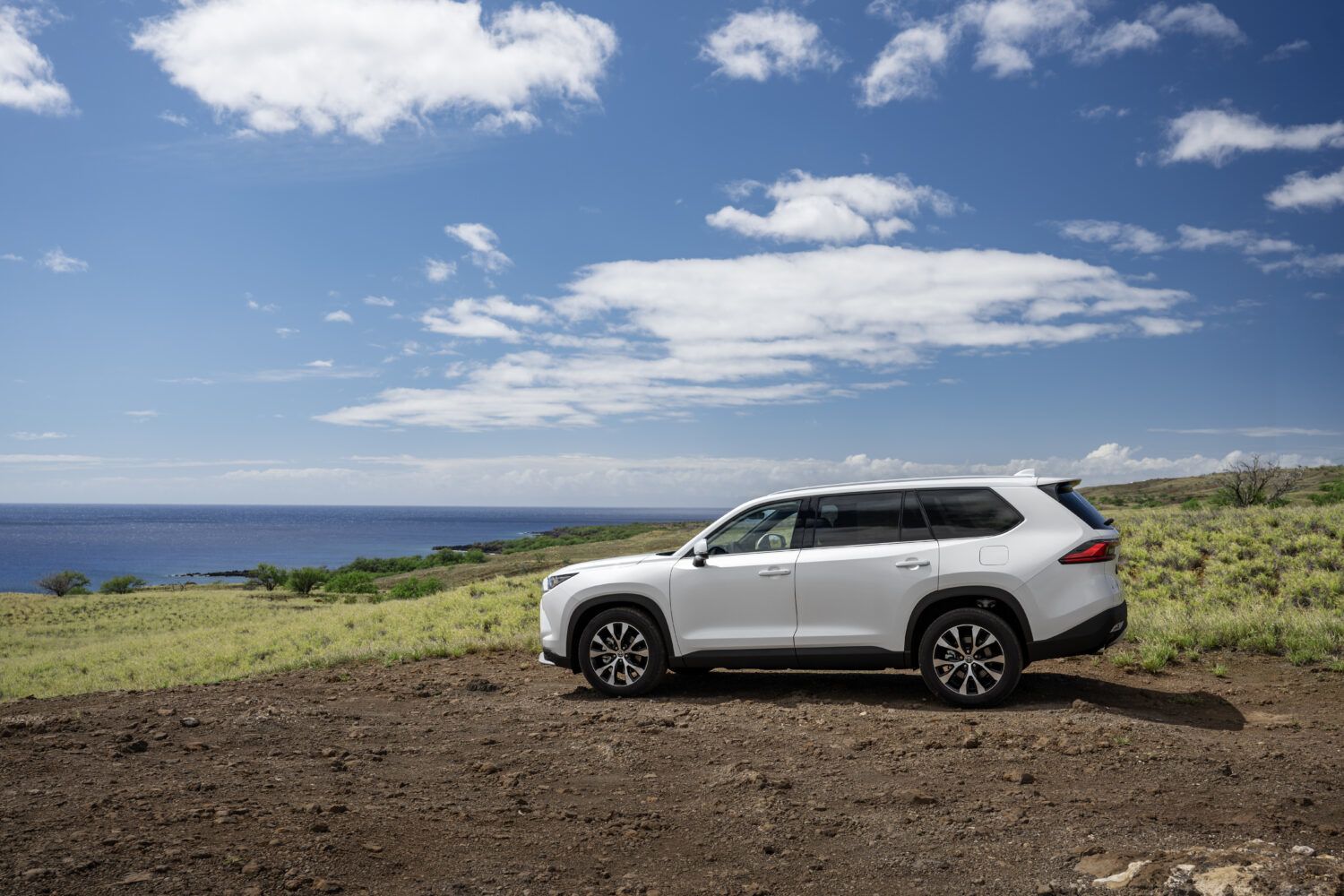 2026 Toyota Grand Highlander - Side view of a white Toyota Grand Highlander parked on a dirt path overlooking the ocean - Georgetown Toyota - New car dealership in Georgetown, Ontario