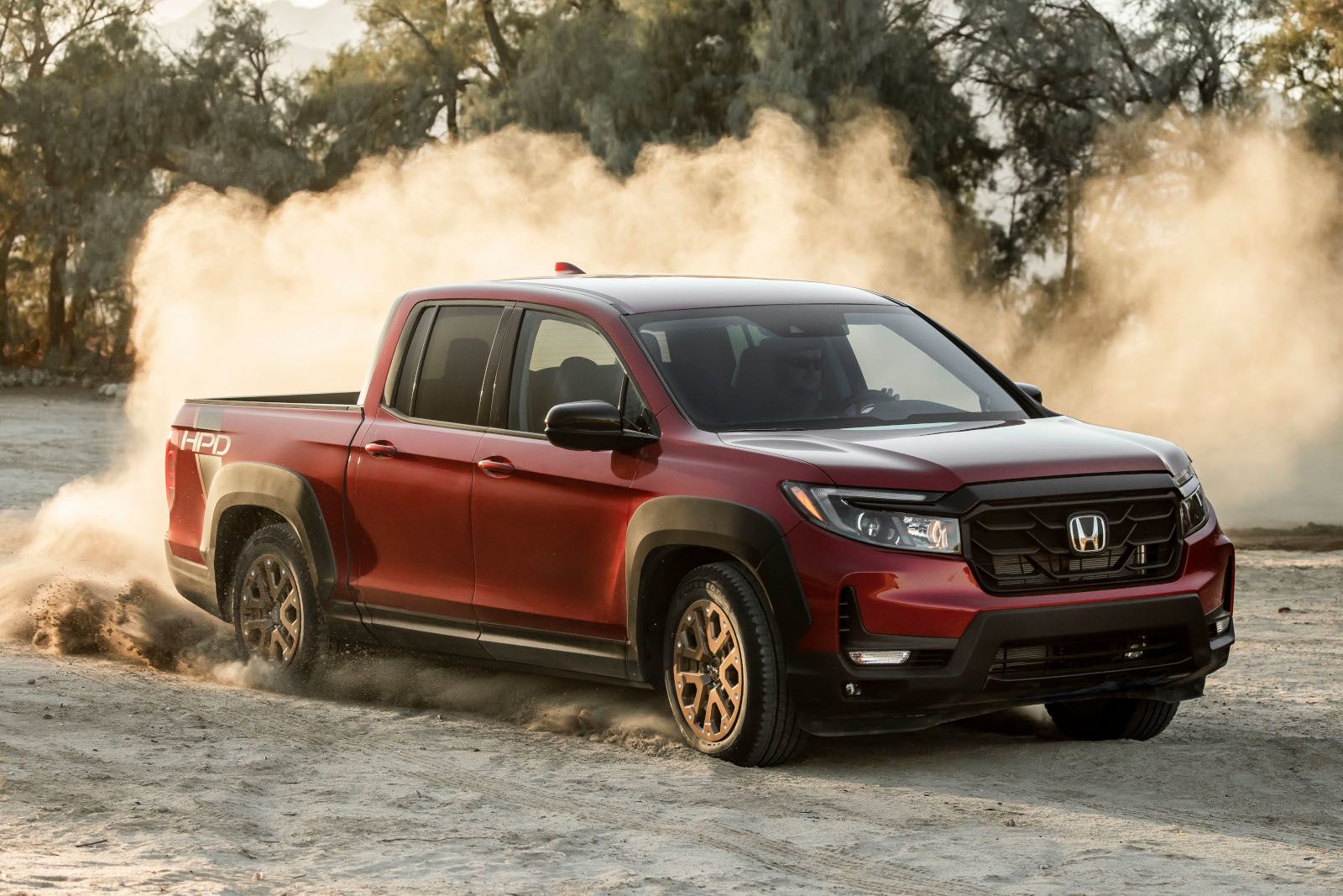 2026 Honda Ridgeline Sport - Front three-quarter view of a red 2026 Honda Ridgeline Sport with HPD package kicking up dust on a dirt terrain - Orangeville Honda - New car dealership in Orangeville, Ontario