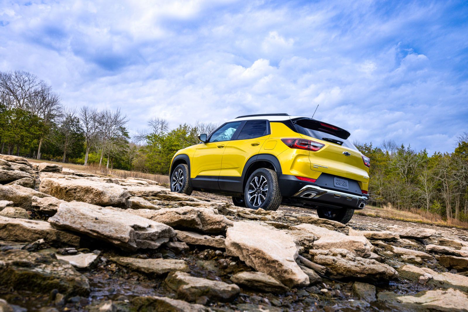 2026 Chevrolet Trailblazer ACTIV - Rear low-angle view of a yellow 2026 Chevrolet Trailblazer ACTIV with a white roof parked on a rocky shoreline - City Chevrolet, Buick, GMC - New car dealership in Toronto, Ontario