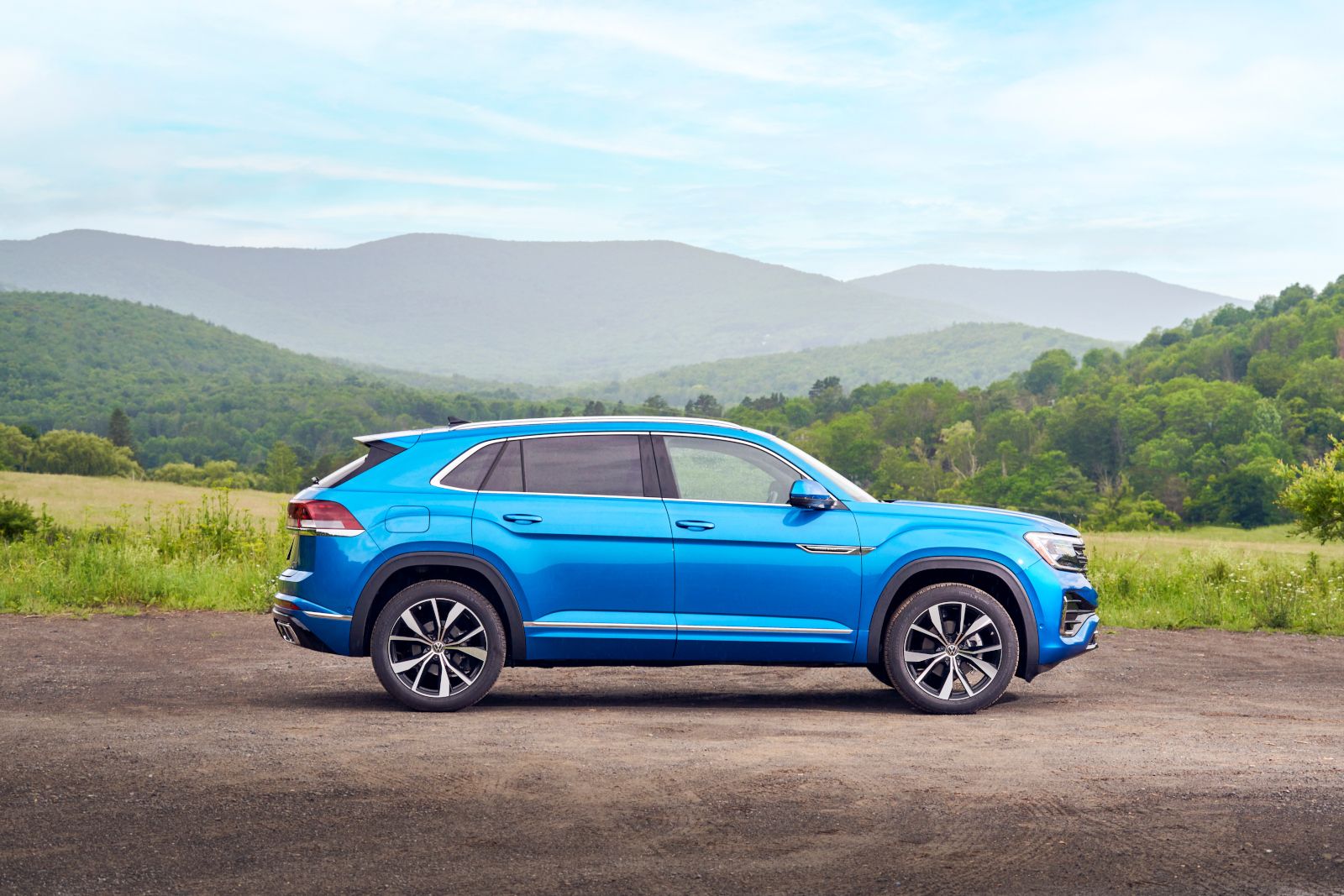 2026 Volkswagen Atlas Cross Sport - side profile view of a blue 2026 Volkswagen Atlas Cross Sport parked in front of green hills - Humberview Volkswagen - New car dealership in Toronto, Ontario
