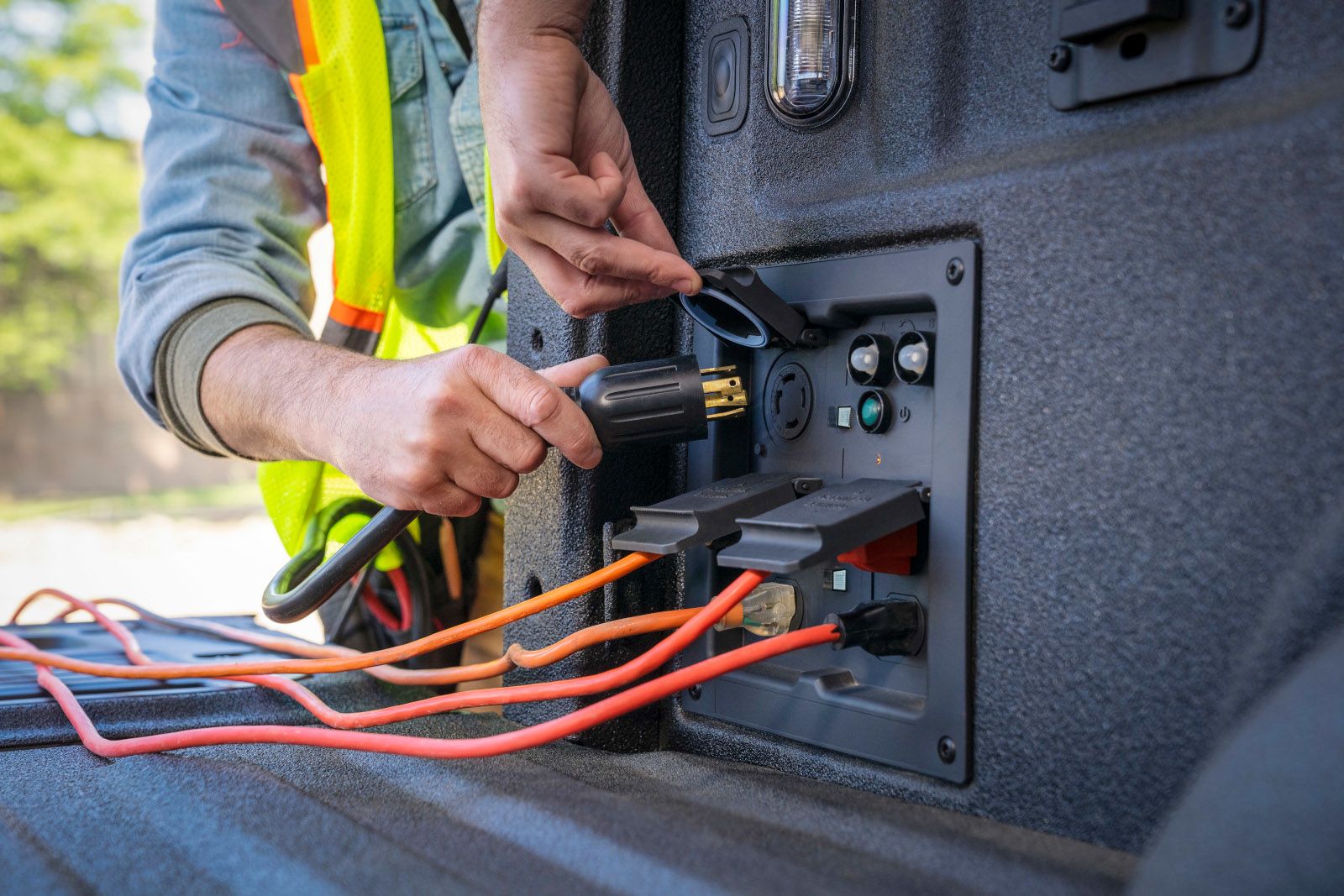 2026 Ford F-150 XLT - close-up view of a person plugging a heavy-duty power cord into the Pro Power Onboard outlet panel in the truck bed of a 2026 Ford F-150 XLT - Mayfield Ford - Ford new car dealership in Brampton, Ontario