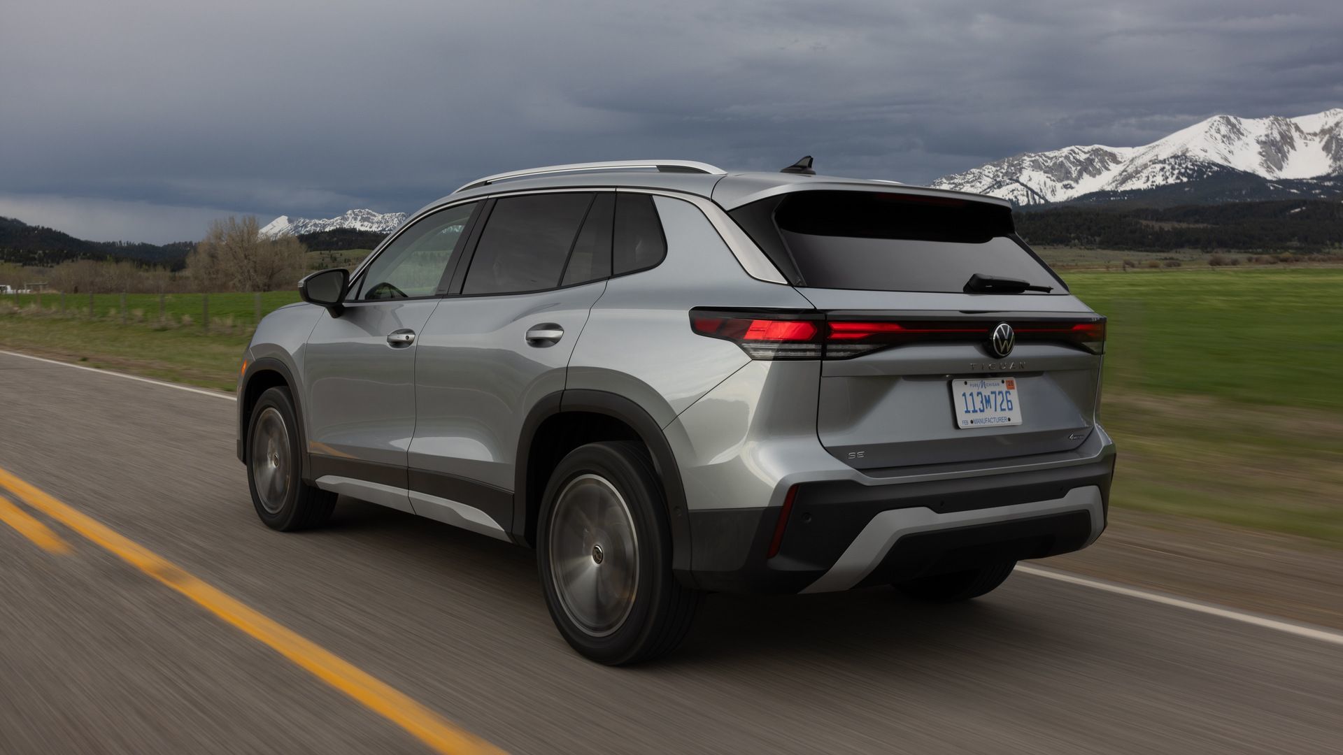 2026 Volkswagen Tiguan - Rear driver-side view of a silver 2026 Volkswagen Tiguan driving on a road - Volkswagen MidTown - New car dealership in Toronto, Ontario