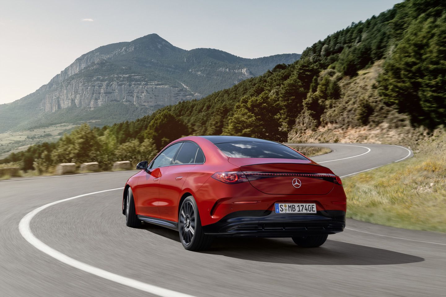 2027 Mercedes-Benz CLA EV - rear view of a red 2027 Mercedes-Benz CLA EV driving on a scenic winding road with mountains in the background - Mercedes-Benz Brampton - New car dealership in Brampton, Ontario