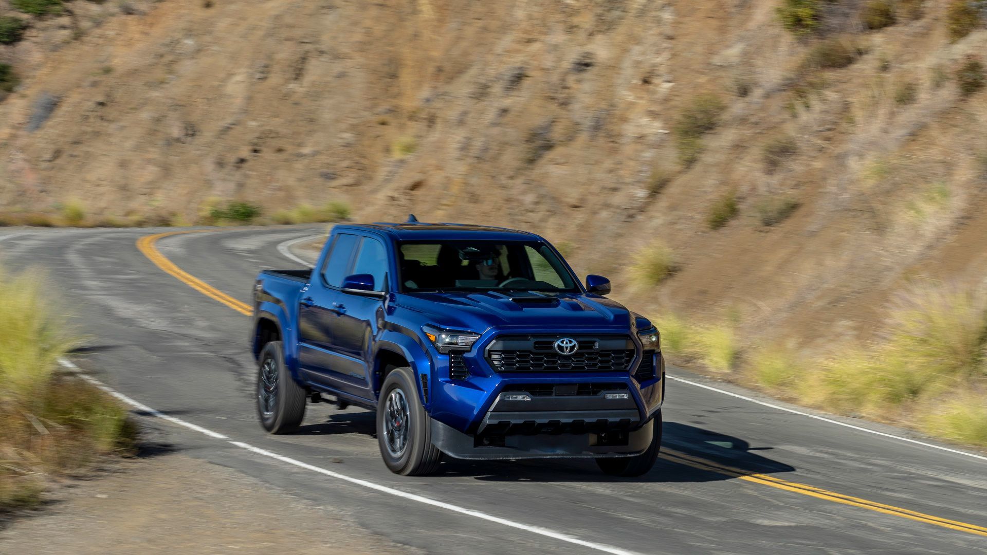 2026 Toyota Tacoma - front three-quarter view of a blue 2026 Toyota Tacoma pickup truck driving on a winding road - Orangeville Toyota - Toyota new car dealership in Orangeville, Ontario