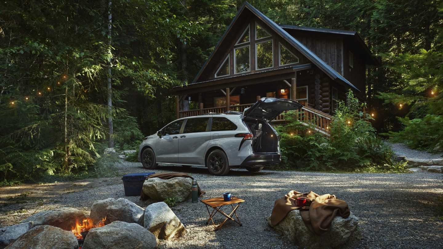 2026 Toyota Sienna - a grey 2026 Toyota Sienna Woodland Edition with its tailgate open parked at a campsite next to a log cabin - Georgetown Toyota - Toyota new car dealership in Georgetown, Ontario