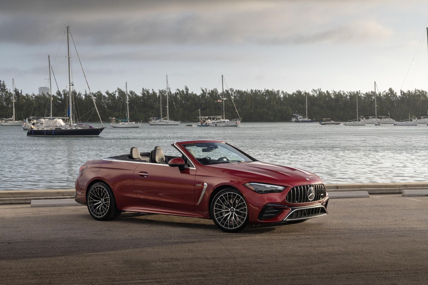 2026 Mercedes-AMG CLE 53 Cabriolet - front three-quarter view of a red 2026 Mercedes-AMG CLE 53 Cabriolet parked near a marina with sailboats - Mercedes-Benz Brampton - Mercedes-Benz new car dealership in Brampton, Ontario