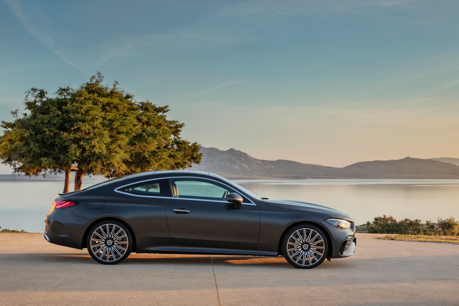 2026 Mercedes-Benz CLE Coupe - side profile view of a matte grey 2026 Mercedes-Benz CLE Coupe parked near a scenic lake with mountains in the background - Mercedes-Benz Brampton - Mercedes-Benz new car dealership in Brampton, Ontario