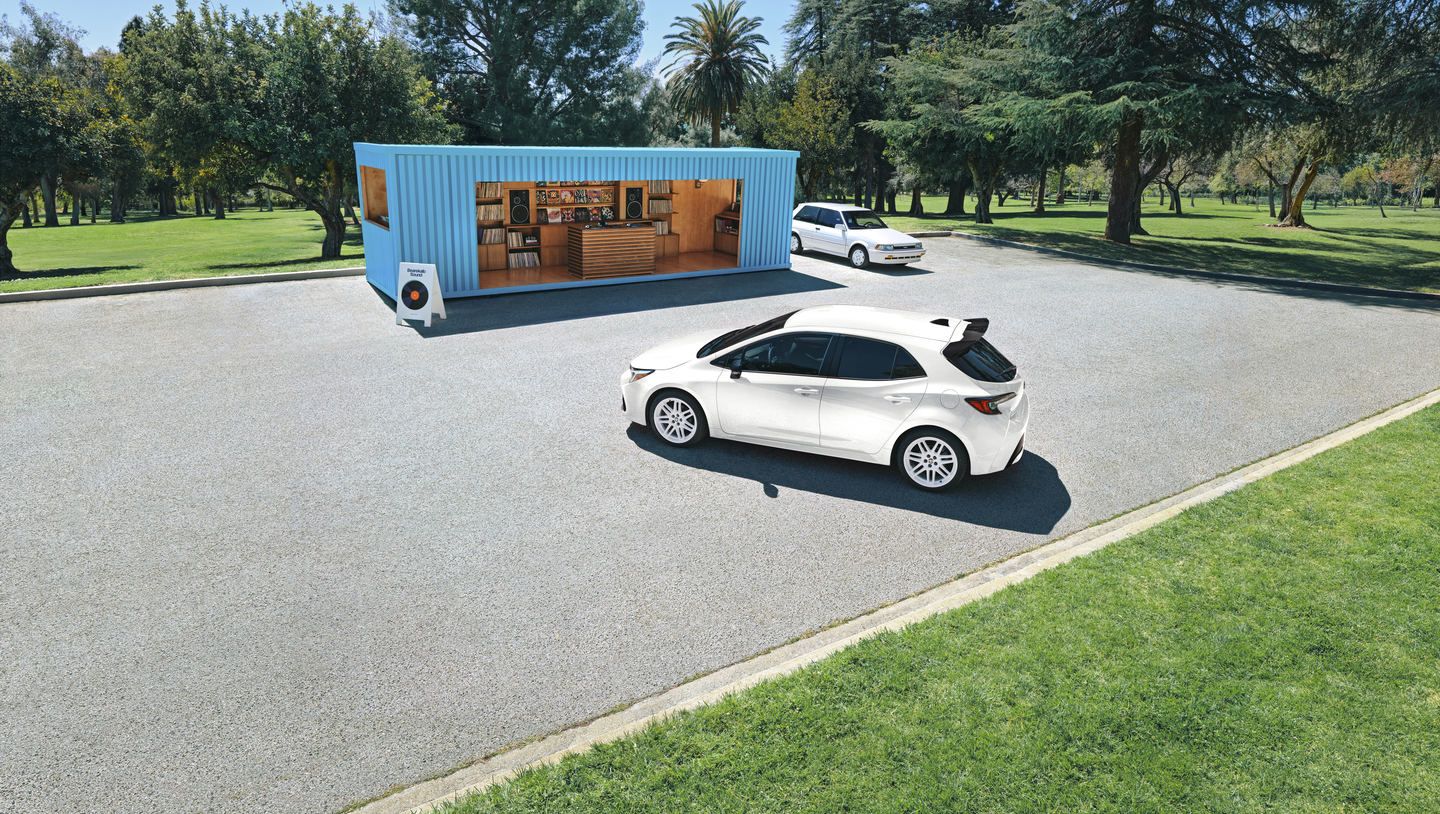 2026 Toyota Corolla Hatchback - a white 2026 Toyota Corolla Hatchback parked outdoors near a blue pop-up shop - Georgetown Toyota - New car dealership in Georgetown, Ontario
